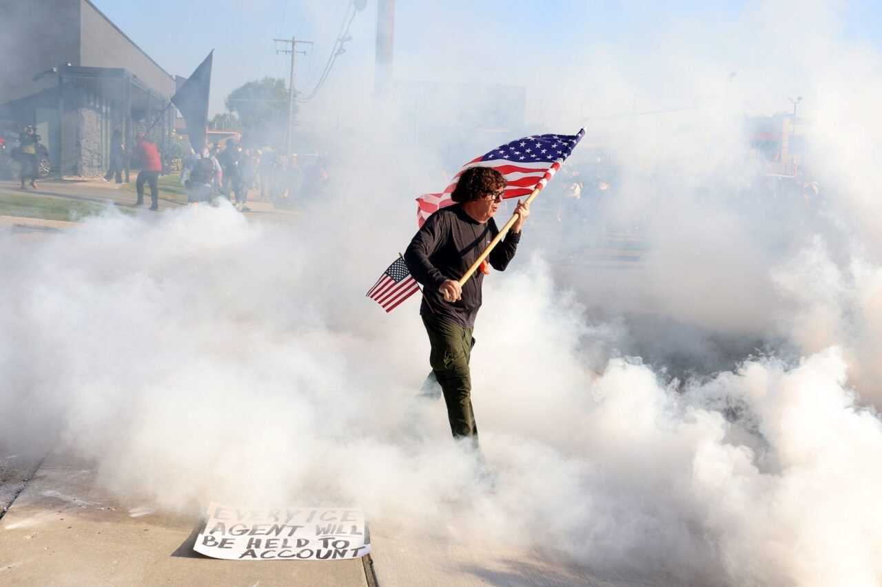 Curtis Evans, of Evanston, carries a U.S. flag through gas deployed by federal officers as they clear protesters from the entrance of the Immigration and Customs Enforcement facility in Broadview, Illinois, on Sept. 19, 2025.
